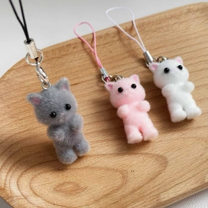Detailed view of three flocked kitten pendants in grey, pink and white on a wooden tray