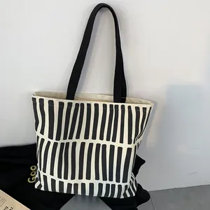 Close-up of a minimalist cream canvas tote bag featuring artistic black vertical stripes