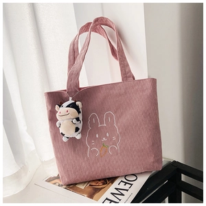 Detail of pink corduroy tote bag featuring rabbit embroidery and a cow plush pendant