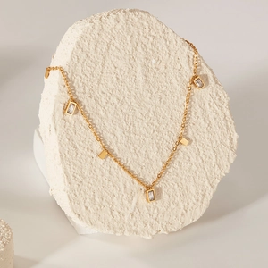 Detailed macro view of a gold chain with rectangular pendants and cubic zirconia on a stone base