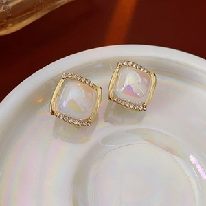 Gros plan de boucles d'oreilles carrées dorées avec opale irisante et halo de diamants