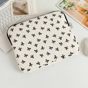 Macro view of cream quilted laptop sleeve featuring black bow patterns and metal zipper