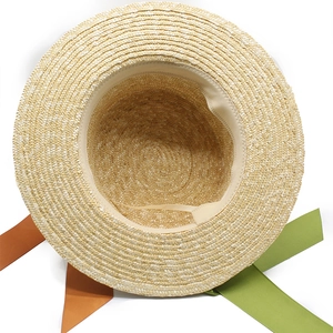 Détail d'un chapeau de paille tissé avec rubans orange et vert sur fond blanc