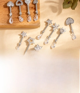 Detail view of silver cartilage piercings with heart and zircon drop pendants on wood