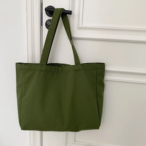 Detail of forest green canvas tote bag showing stitching quality on a door handle