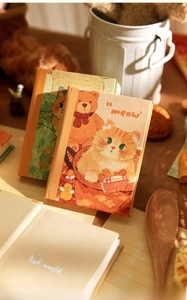 Close-up of A7 notebook with cute cat illustration and 'kittens save the world' text