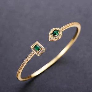 Elegant gold open bangle with green square and pear-shaped gemstones and crystal pavé