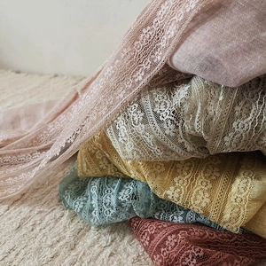 Close-up detail of delicate floral lace patterns on colorful linen scarves stacked neatly