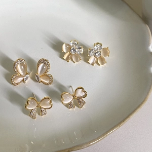 Golden bow pearl earring set with cat eye stones and sparkling crystals on white plate