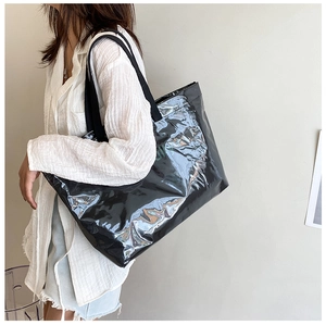 Detail of a large black glossy jelly tote bag worn on shoulder by a model