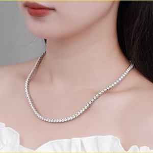 Close-up of a silver tennis necklace with four-claw set moissanite diamonds on a model