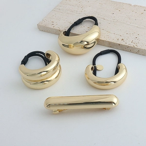 Close-up of gold metal hair clips and elastic bands on a minimalist stone plate