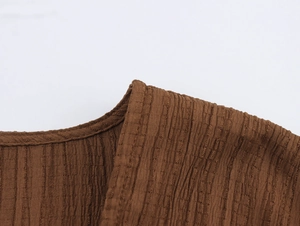 Detail view of dark brown smocked fabric with vertical rib texture and neat neckline piping