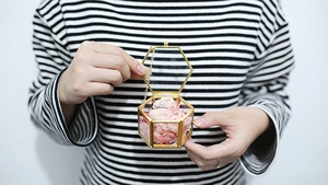Close-up of hexagonal glass jewelry box with gold trim and pink flowers inside