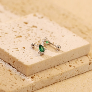 Macro shot of silver studs with emerald green pear-shaped gems and screw-back detail