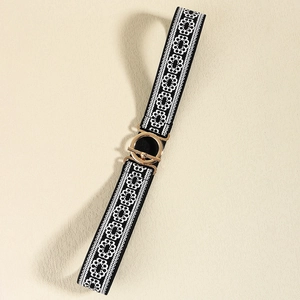 Detail of black elastic belt with white geometric embroidery and gold round metal buckle