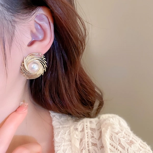 Detailed view of a gold spiral earring with a large center pearl worn by a model