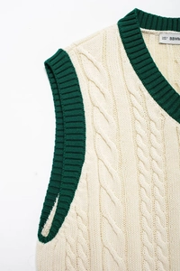Detailed knit texture of V-neck cable vest with green ribbing on cream fabric