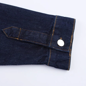 Détail du poignet en jean bleu foncé avec coutures orange et boutons en métal argenté