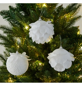 Close-up of white petal-textured Christmas baubles with glitter on a lit tree branch
