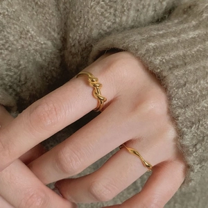 Close-up of dual gold spiral and wavy rings worn together on a knit background