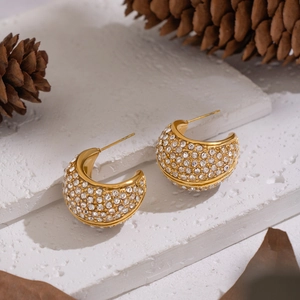 Detail of C-shaped gold-plated hoop earrings with pavé set rhinestones on a rustic base