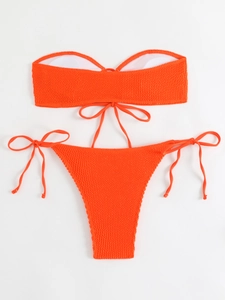 Detailed flat lay of vibrant orange bandeau bikini set with ribbed waffle texture and ties