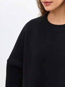Detail of ribbed crew neck and drop shoulder seam on a thick black cotton sweatshirt