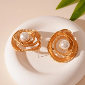 Macro view of golden spiral flower earrings with pearls on a minimalist white stand