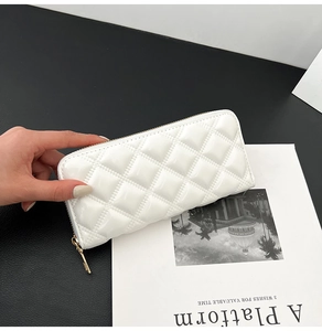 Detail of white quilted patent leather clutch purse with metal zipper on a magazine