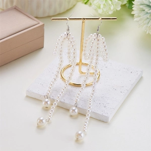 Detail of bow-knot pearl earrings with golden tassels on a jewelry display stand
