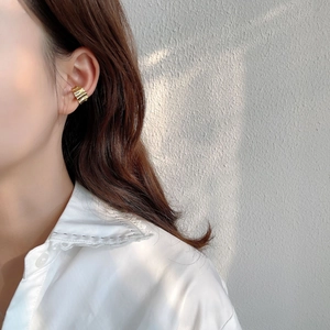 Close-up of golden wavy ear cuff showing metallic texture on model with natural lighting