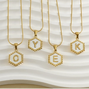 Detail of 18k gold snake chain necklaces featuring hexagonal white shell initial pendants