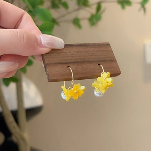 Detail showing handmade osmanthus flower earrings with white pearls on a wood stand