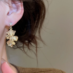 Close-up of golden ginkgo leaf earrings with zircon stud worn by a female model
