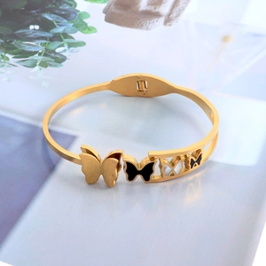 Minimalist gold butterfly open bangle with black and white inlay on a plant motif backdrop