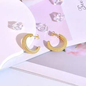 Close-up of golden C-shaped hoop earrings featuring a sophisticated woven mesh texture