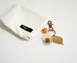 Detail of cute milk tea bear keychain with pineapple bun charm on canvas bag accessory