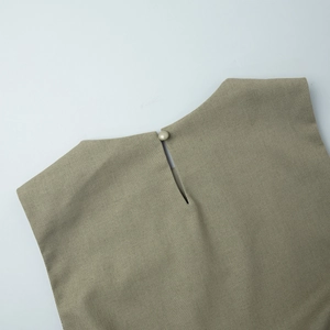 Detail view of the round neckline with a button closure on a light green cotton linen top