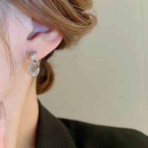 Close-up of twisted silver metal hoop earring worn by a model in a minimalist style