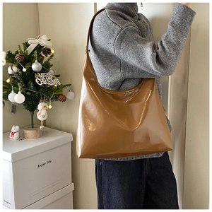 Dettaglio di una borsa hobo marrone lucida indossata da una modella in interno