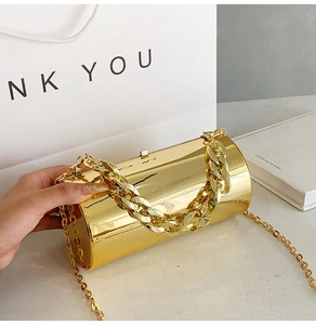 Close-up of golden cylindrical evening clutch bag with metallic mirror finish and chain