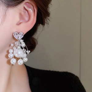 Dettaglio macro di orecchini in argento con perle, cuore in zircone e frange di perle