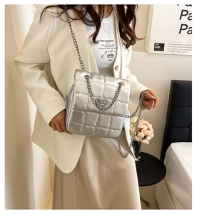 Close-up of quilted silver chain bag with a heart-shaped metallic clasp detail