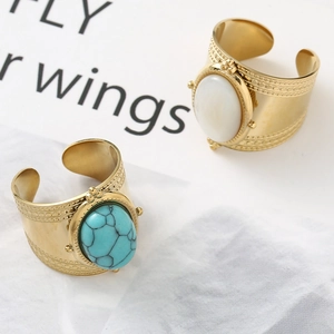 Detail of gold-plated wide rings with turquoise and white stones on white satin fabric