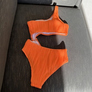 Detail of orange one-shoulder cutout swimsuit with textured ribbed stretch fabric