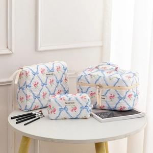 Three-piece quilted floral makeup bag set with ribbon bow patterns and a brand label