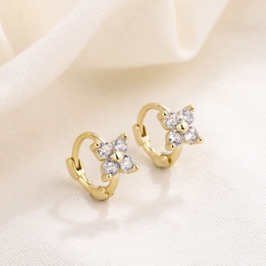 Macro detail of gold four-petal flower earrings with sparkling cubic zirconia on linen