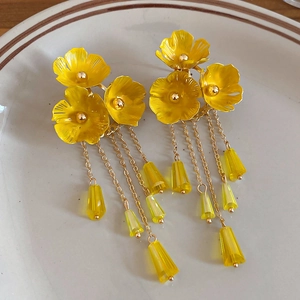 Detail von gelben Blumenohrringen mit goldenen Quasten auf einem weißen Keramikteller