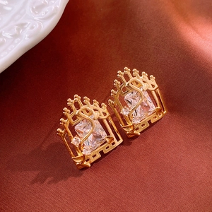 Close-up of golden square zircon earrings with swan motif on elegant red silk fabric